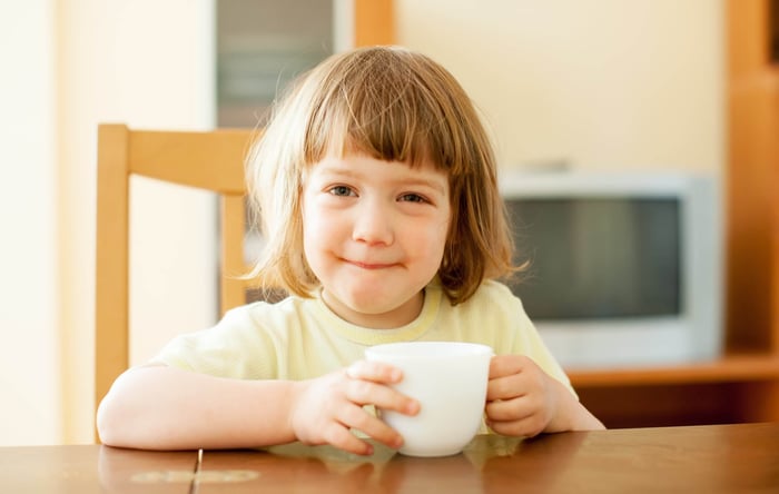 Child holding a cup of drink in the kitchen in the morning