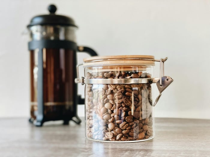 Glass jar filled with coffee beans next to a French press