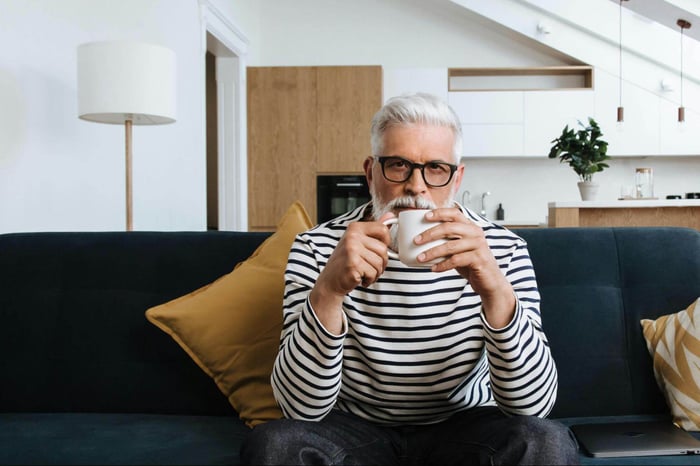 Elderly man with gray hair sipping coffee on cozy living room sofa