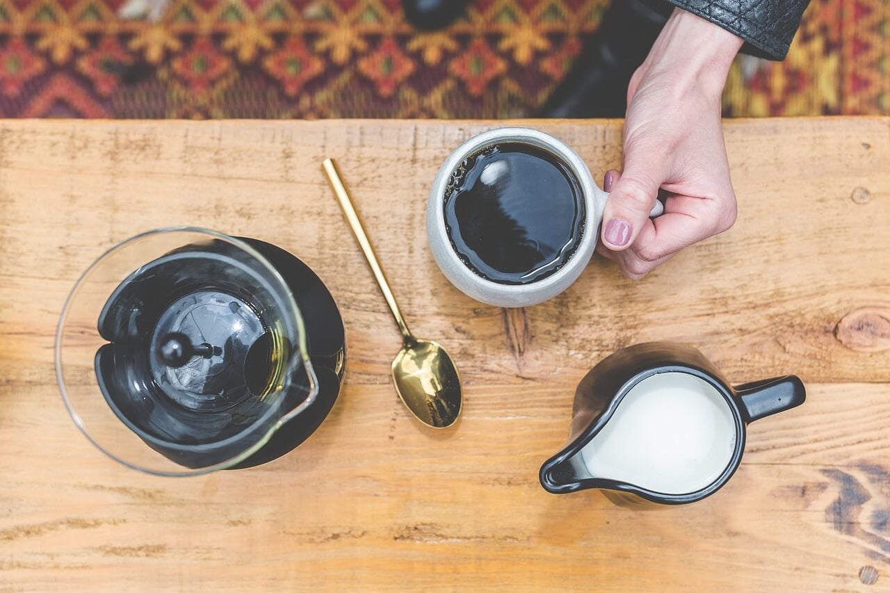 Hand holding black coffee with milk pitcher.