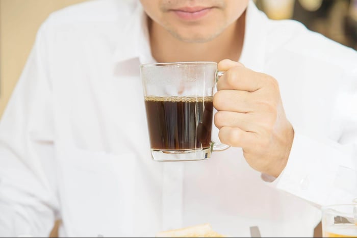 man holding cup of black coffee near face