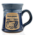 The front of the Bones Coffee Company Megalodonut Handthrown Mug. It has the Megalodonut art on the golden medallion. The mug is navy colored with a grey and white glaze.