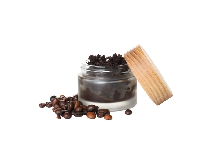 Used coffee grounds in clear container with coffee beans on the side.