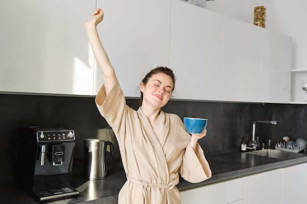 women with coffee cup stretching arms in kitchen