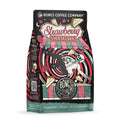 The front of a 12 ounce bag of Bones Coffee Company Strawberry Cheesecake coffee. Its flavor is strawberry cheesecake, and it has a skeleton with a button-down shirt falling into a red and white swirl with cheesecake and strawberries on the art.